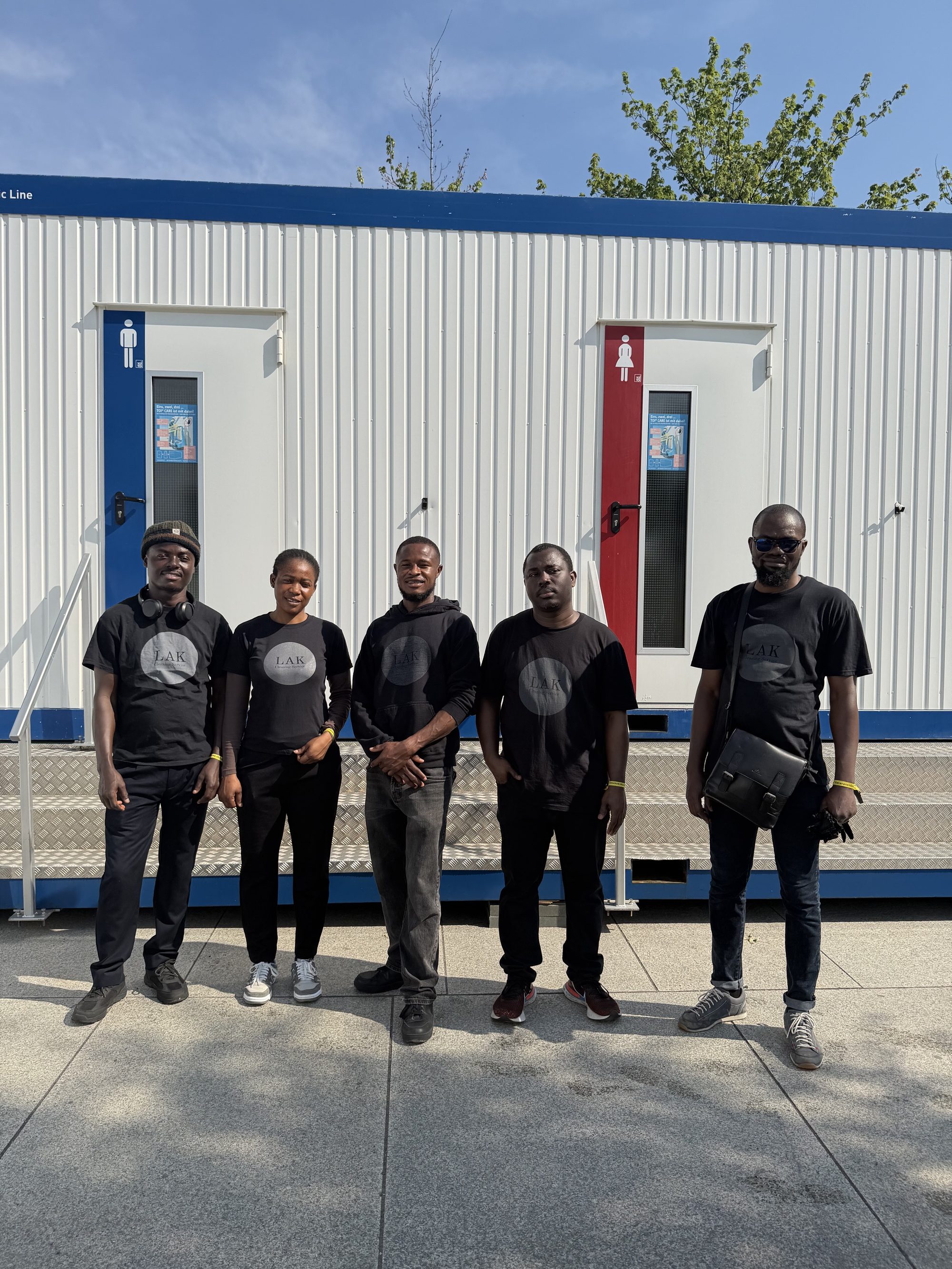 LAK Cleaning Service Team – fünf Mitarbeiterinnen und Mitarbeiter in schwarzen Teamshirts vor Sanitärcontainern beim Deutschen Veteranentag in Berlin